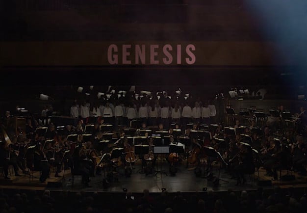 Utdrag ur filmen Genesis. Stor orkester och upplyst i bakgrunden med tetxen Genesis. Fotografi.