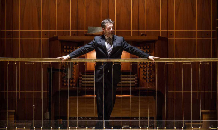 Man stående mot räcket fram en orgel. Fotografi.